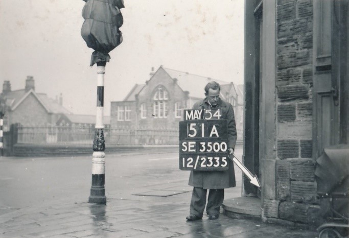 alt="man in overcoat with sign board and arrow at crossroads"