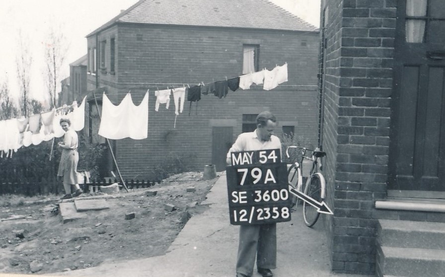 alt="man with sign board and arrow with woman hanging washing out behind"