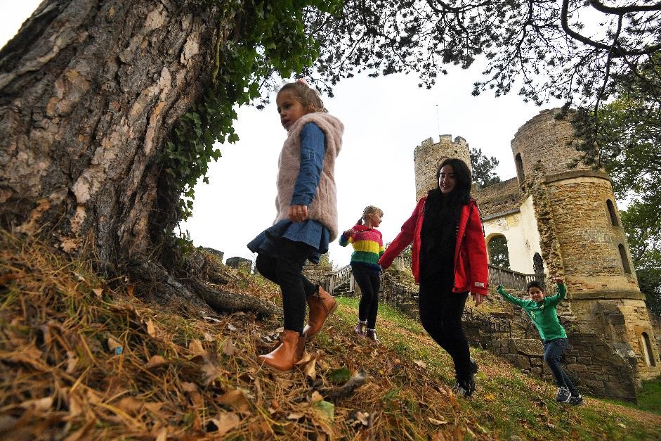 alt="four children searching for geocache underneath large tree with castle ruins behind"