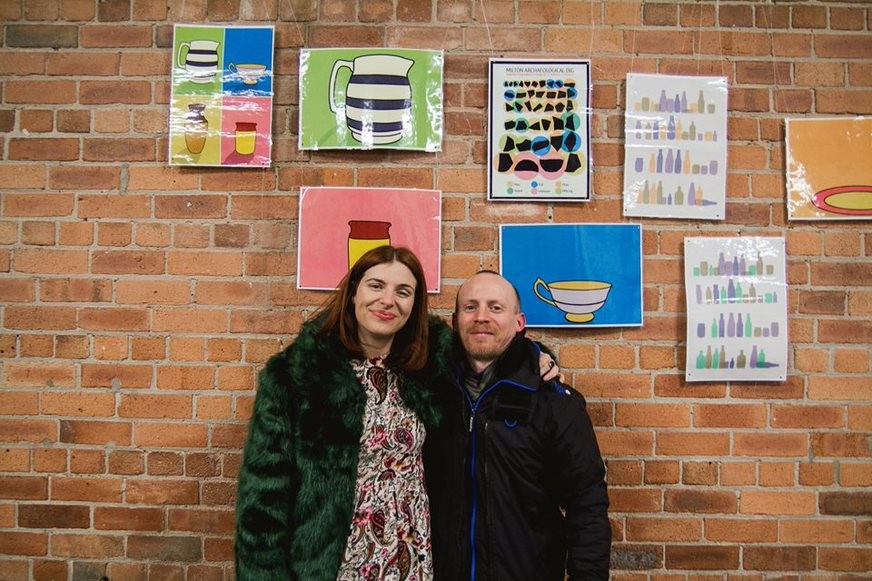 two people in front of brick wall decorated with colourful artwork
