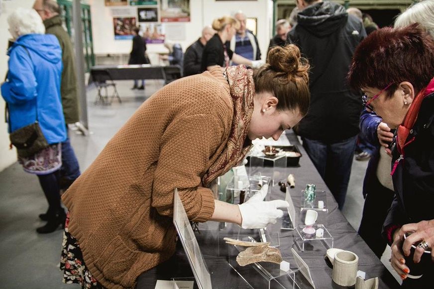 archaeologist with white gloves showing objects on a table to members of the public