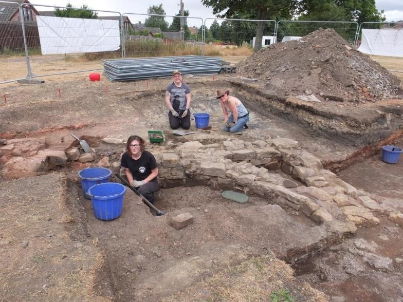 three people with tools and buckets kneeling next to stone foundations