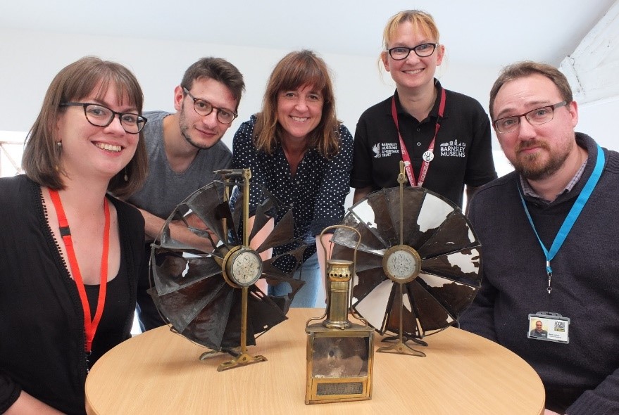 five people in front of a round table with two round fans and a brass lamp on