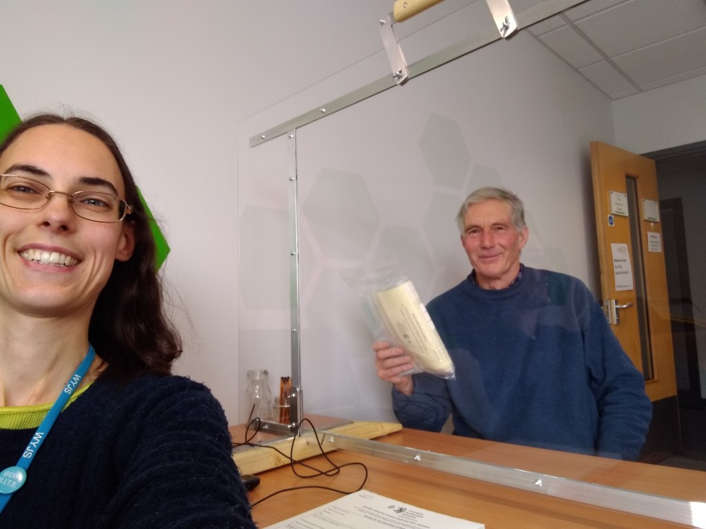 Finds liaison officer and object finder at a desk with a screen in between them. Both are smiling at the camera.