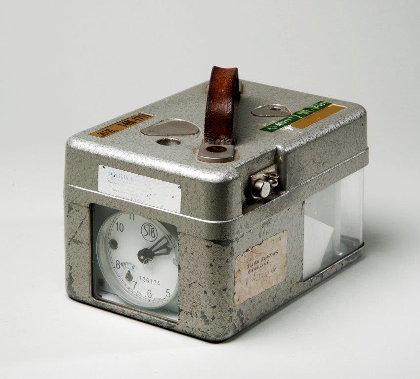 A grey box with a small clock on the front and a carry handle on top