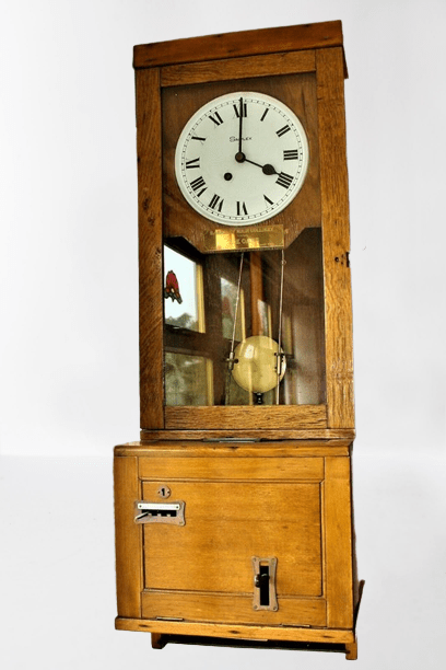 A pine clocking in machine, with a white clock face and pendulum. The base has an insert for a piece of paper.