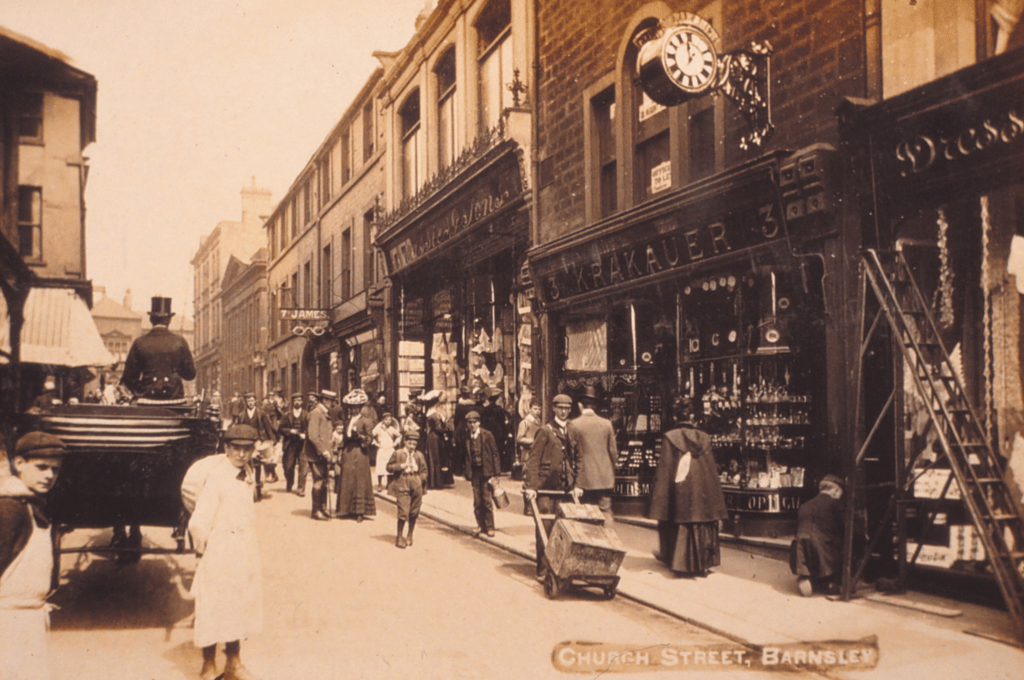 A sepia photo showing a busy Church Street in the town centre. The Krakauer shop is in the foreground and above the entrance is a clock