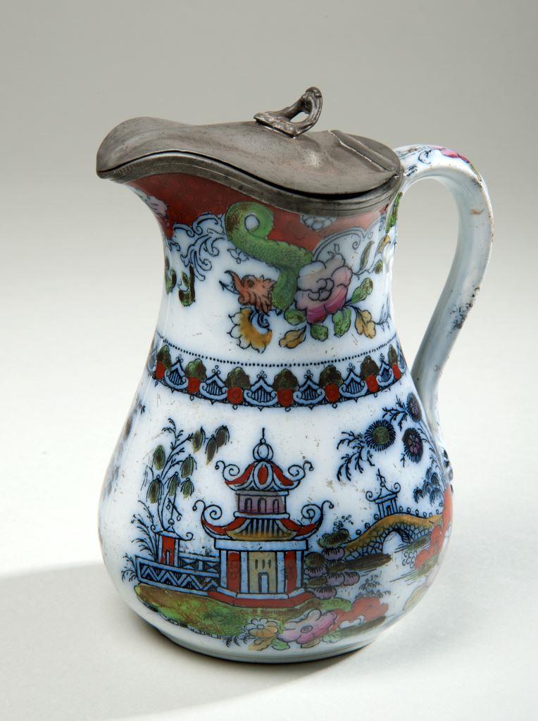 The jug mimics symbols from cultures within China, Japan, and other East-Asian countries. The jug has a transfer-printed design with pagodas, bridges, red and pink flowers, as well as green dragons near the top of the jug