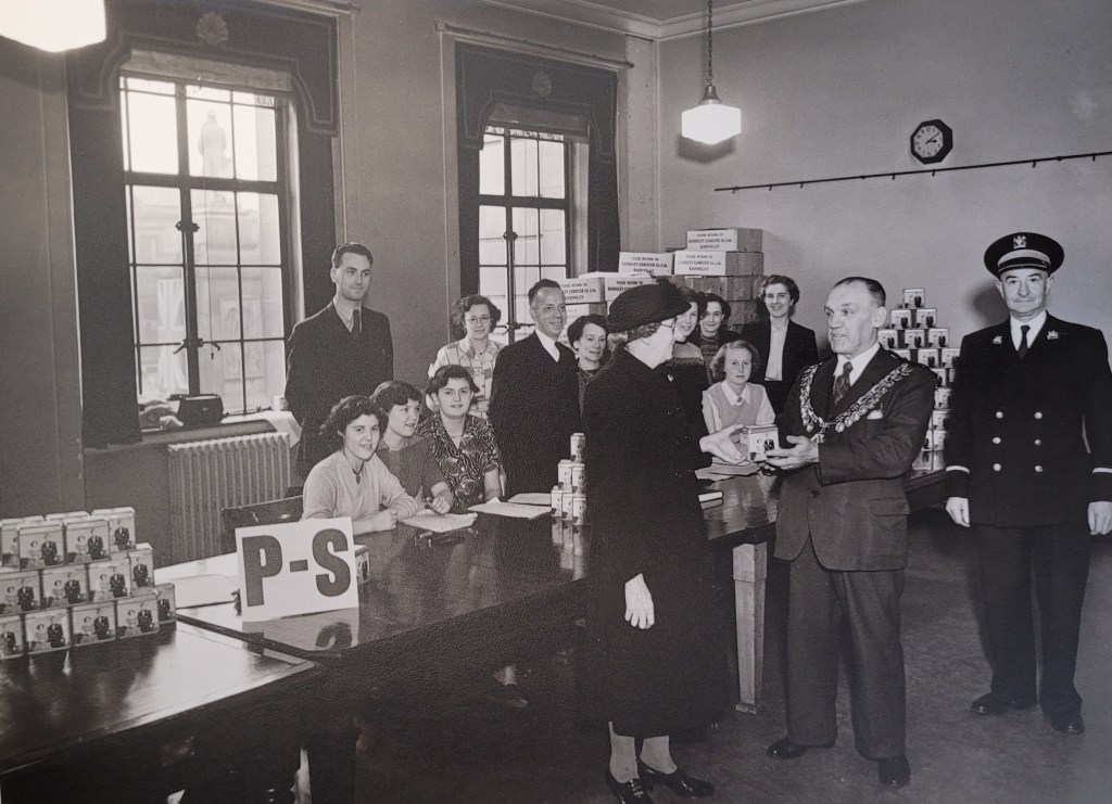 People standing around a table in the Barnsley Town Hall, where there is a stack of commemorative tins