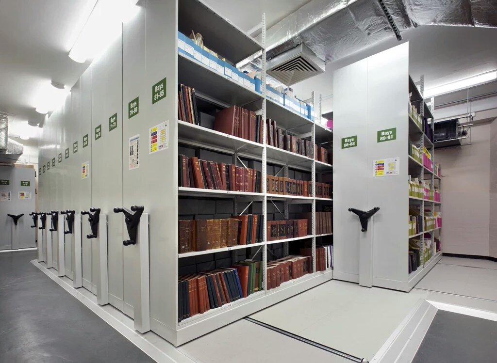 A store room in the basement of the town hall, one of the racks is open showing 4 shelves of books