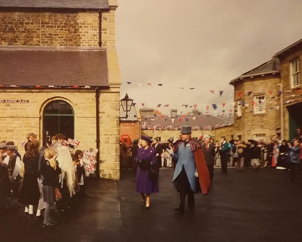 Queen Elizabeth walking across the courtyard at Elsecar Heritage Centre in front of waiting crowds waving union jack flags