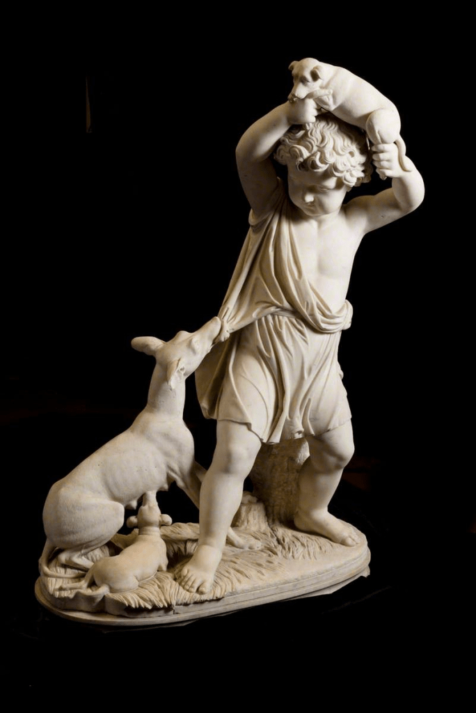 Marble sculpture in the round of a young male figure in classical dress. There is a dog pulling at his clothing and he holds a puppy above his head.