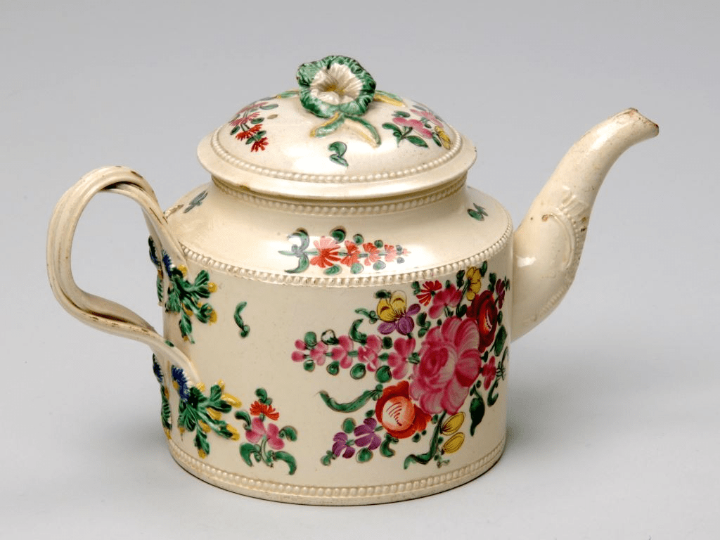 A ceramic teapot and lid made from creamware. The teapot has a twisted two strand handle and moulded spout. The lid has a moulded flower finial. The whole is hand painted with flowers and foliage in green, yellow, pink and red. 