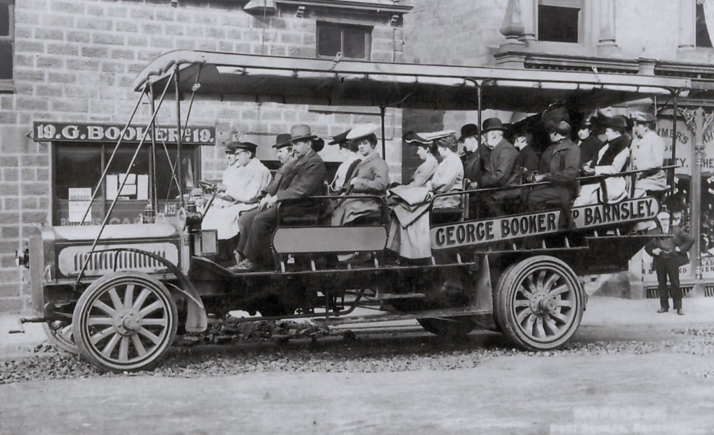 A charabanc filled with people. The building behind says 19 G Booker