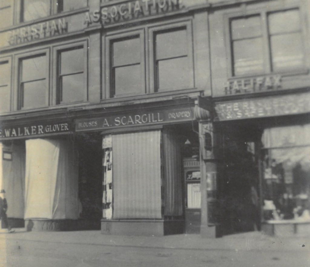 Photograph showing the detail of the shopfronts on the ground floor. The shop signs say Walker (Glover) A Scargill (Blouses and Drapery). A Halifax sign is visible on the next door building.