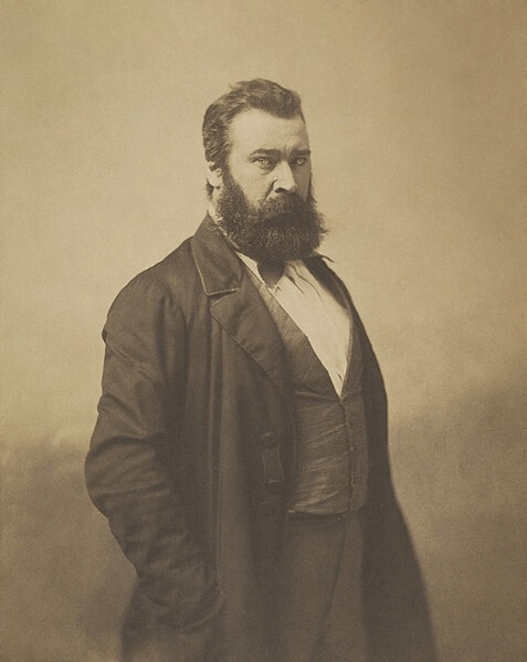 A photograph of Millet who has a bushy beard and is wearing a long coat