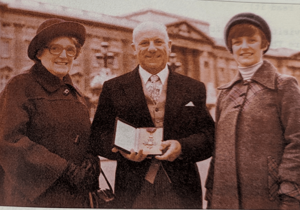 Stanley holding his medal towards the camera, two ladies are stood either side of him
