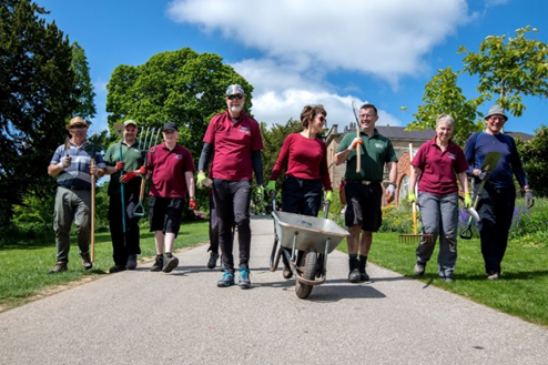 a group of volunteer walking towards camera, carrying tools and pushing a wheelbarrow