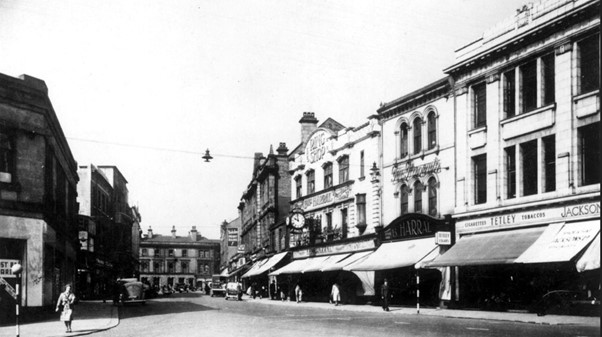 black and white photograph of Eldon Street showing 32-38. All of the shops have pull out awnings. The new building at 36-38 is visible and has two signs that say 'Tetleys cigarettes tobaccos' and 'Jacksons'