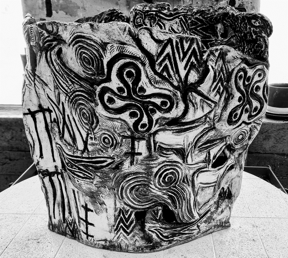 Black and white photo of a ceramic pot with intricate, abstract designs featuring geometric patterns, swirls, and symbols. 