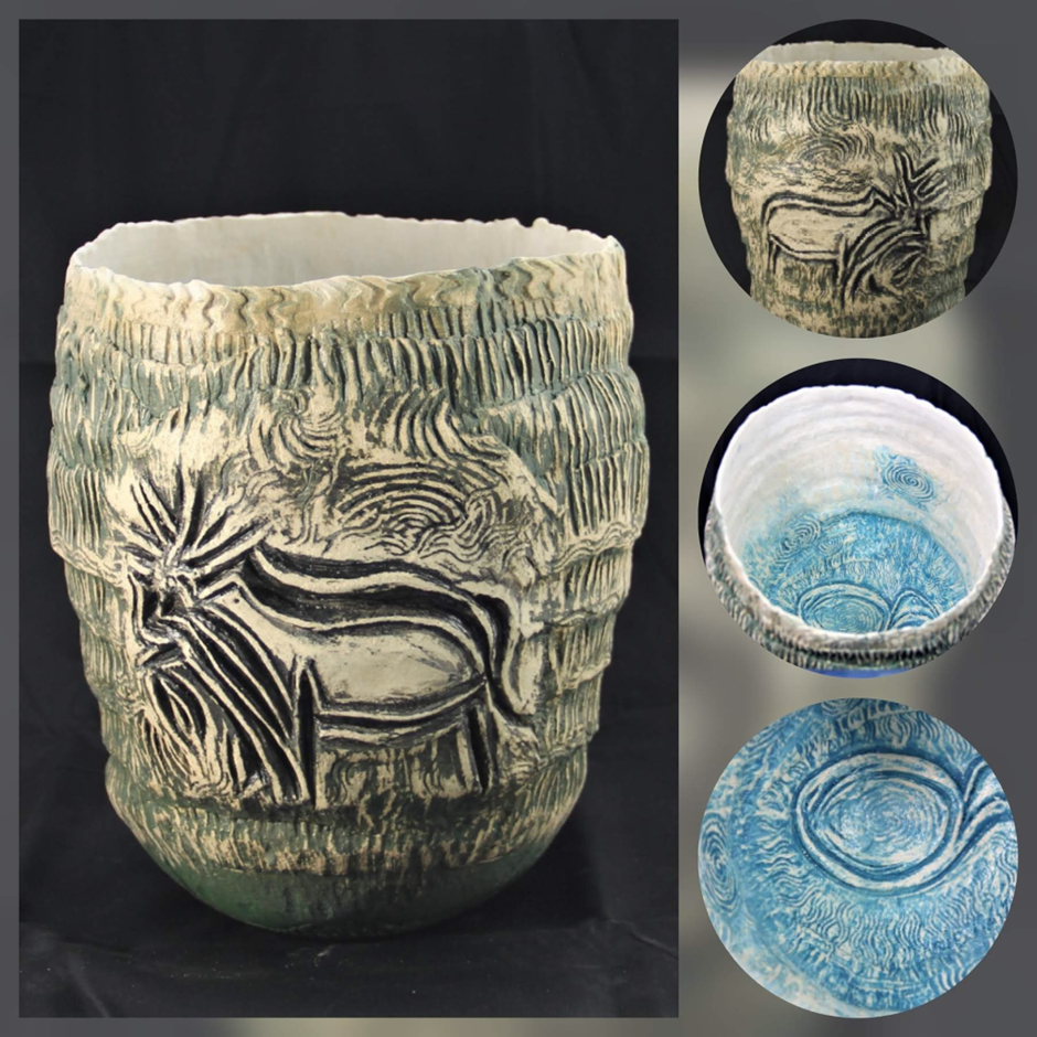 A clay pot featuring an intricate design of a reindeer on its surface. The pot has a textured exterior with a gradient from dark green at the base to light cream at the top. Inside, the pot has a detailed blue and white pattern.