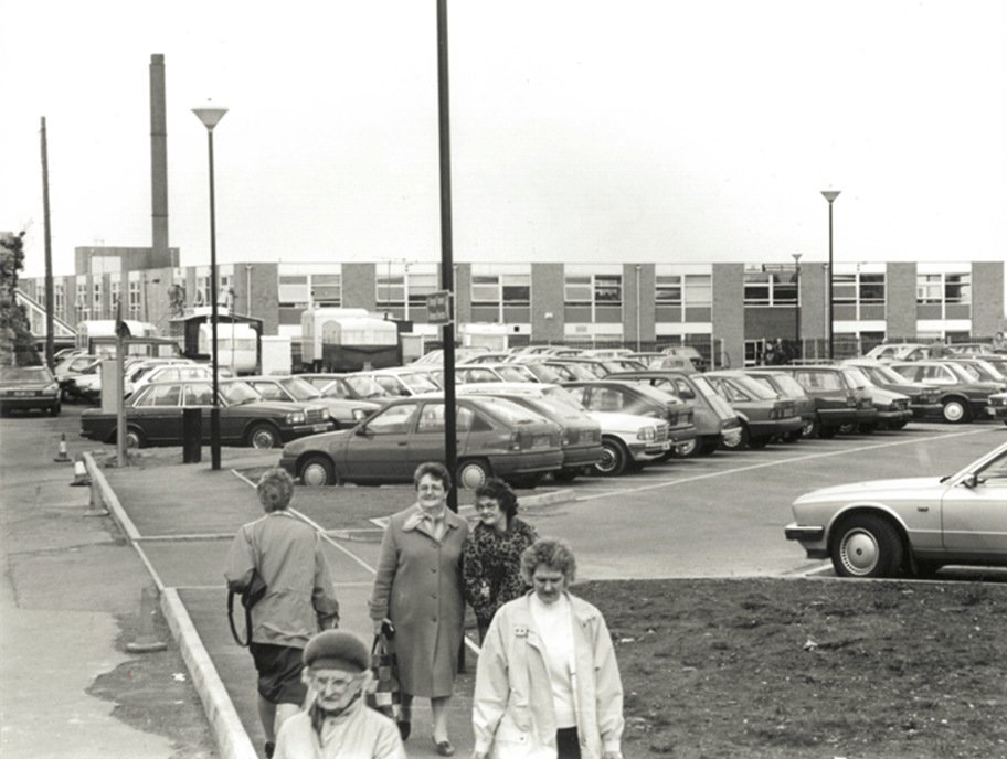 Council offices in background, situated behind cars in a car park. A group of people walking on pavement in foreground.