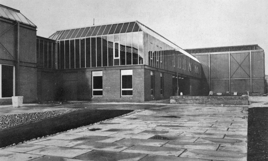 A partly brick building with glass areas and paved areas. Taken from the outside.