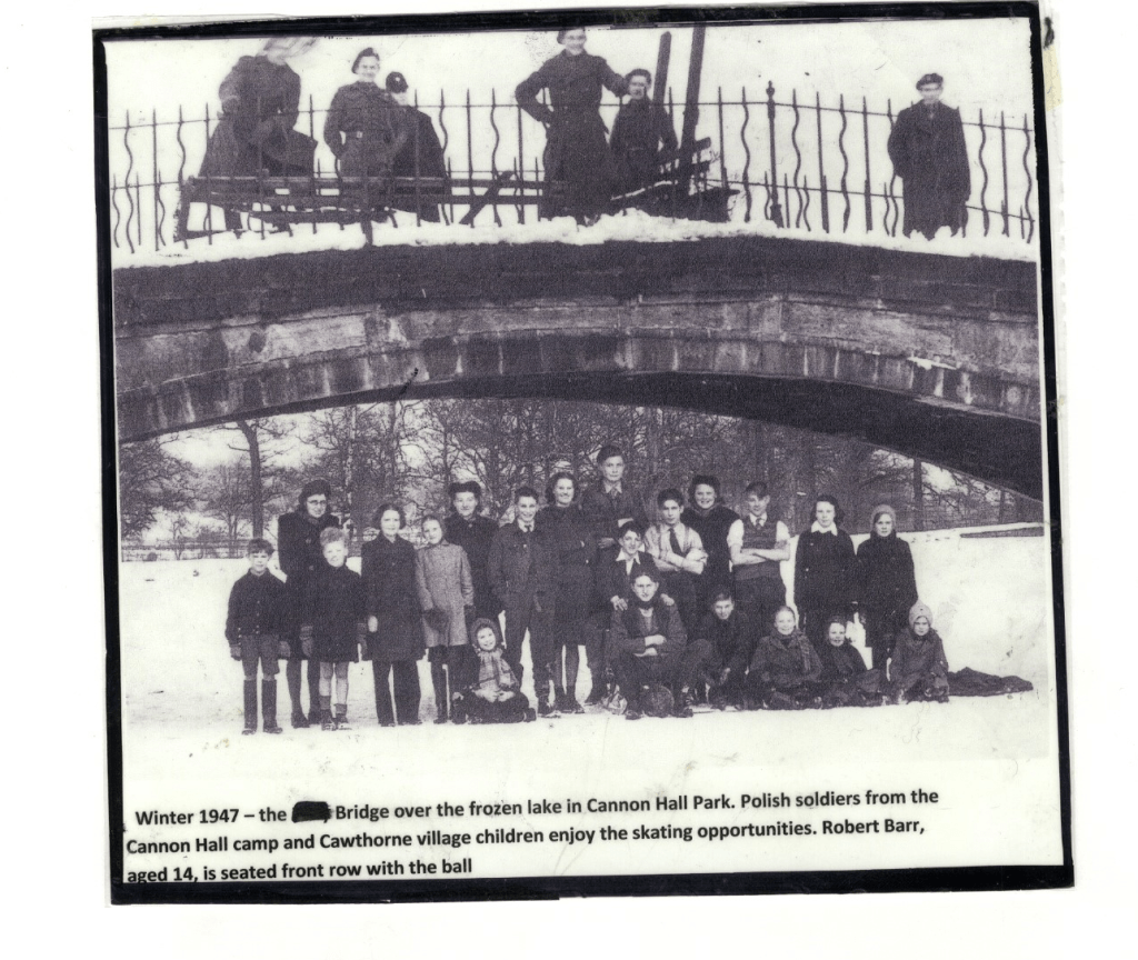 Black and white photograph of people on and beneath a snow-covered bridge over a frozen lake in Cannon Hall Park during winter in 1947. Soldiers and children, including Robert Barr seated with a ball in the front row, enjoy the skating opportunities.