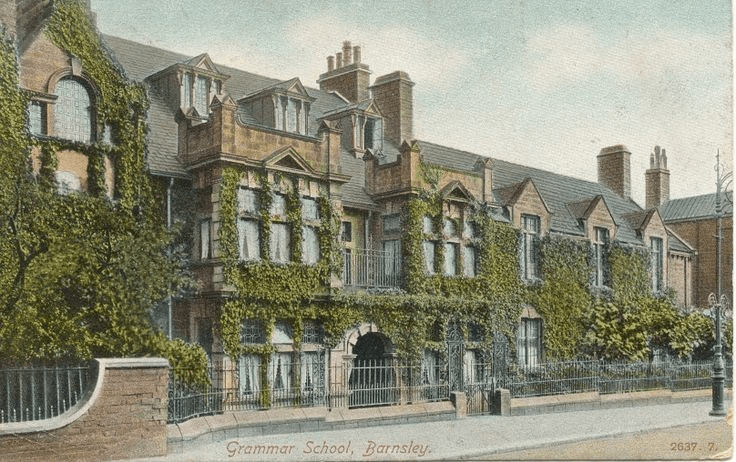 A vintage postcard features the ivy-covered facade of the Grammar School in Barnsley. The building has multiple windows, three stories, and peaked roofs. A wrought iron fence stands in front, with leafy vines climbing the brickwork. The caption reads “Grammar School, Barnsley.”.