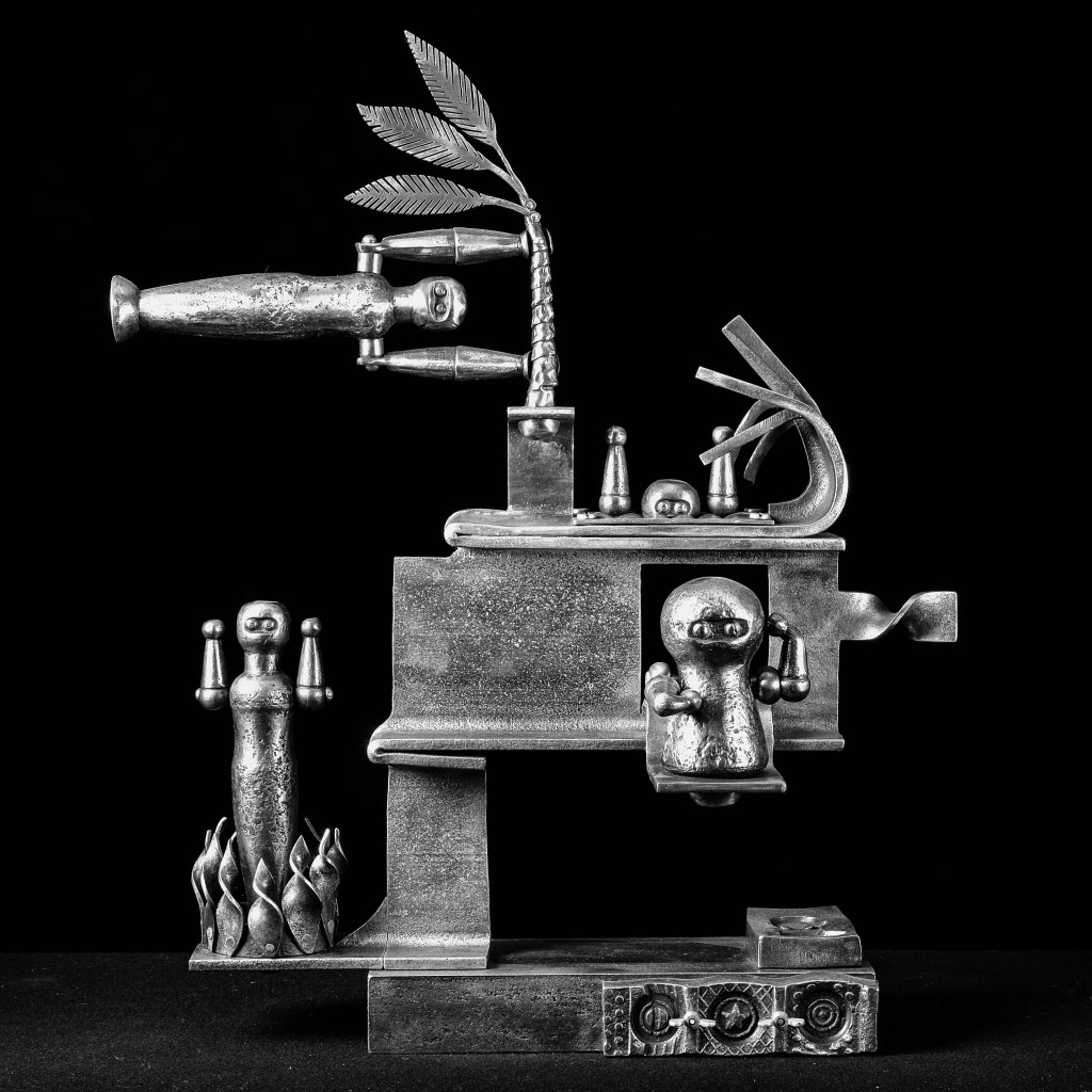 Abstract metal sculpture with various shapes and figures. Features include human-like forms holding dumbbells, a palm tree-like element, and intertwined tendrils, all on a multi-level metallic structure set against a black background.