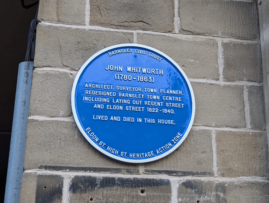 A blue plaque on a brick wall commemorates John Whitworth (1780-1863), an architect and surveyor. He redesigned Barnsley town center, including Regent Street and Eldon Street. He lived and died in this house.