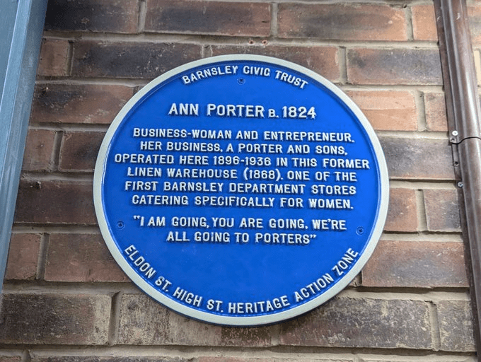 A blue historical plaque on a brick wall for Ann Porter, born 1824. It details her as a businesswoman and entrepreneur in Barnsley, running a department store from 1896 to 1936 in a former linen warehouse. The plaque is by Barnsley Civic Trust.