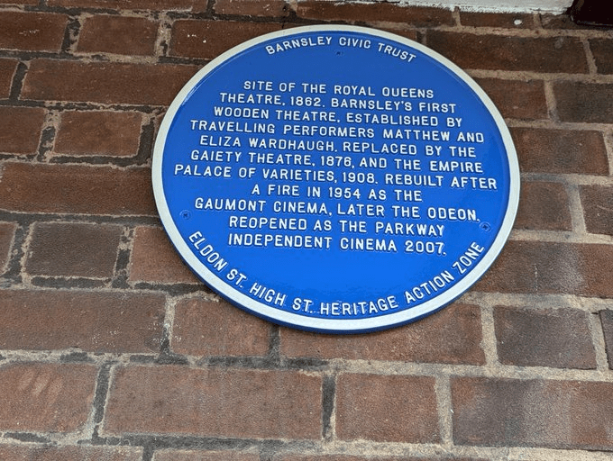A blue plaque on a brick wall commemorating the site of the Royal Queens Theatre in Barnsley, detailing its history from 1862, changes over the years, and its current status as the Parkway Independent Cinema since 2007.