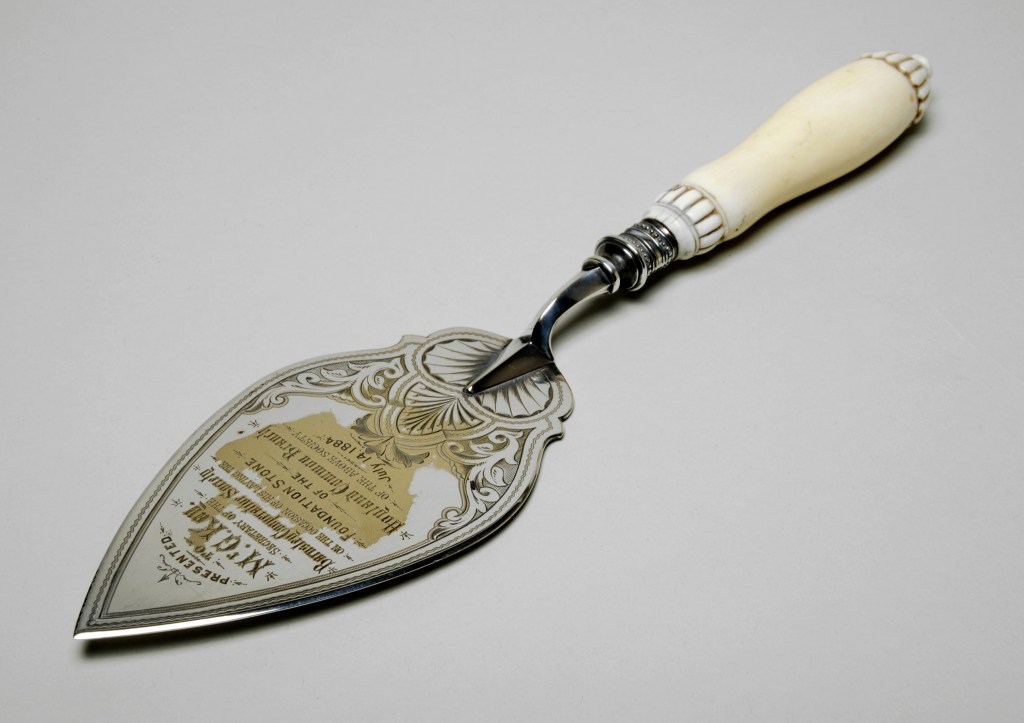 A commemorative trowel with an ornate metal blade and an ivory handle, inscribed for the laying of a foundation stone by Mr. G Kay in 1884.