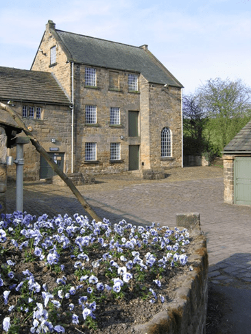 Exterior view of Worsbrough Water and Steam Powered Flour Mill, showcasing its stone architecture and surrounding flowering plants.