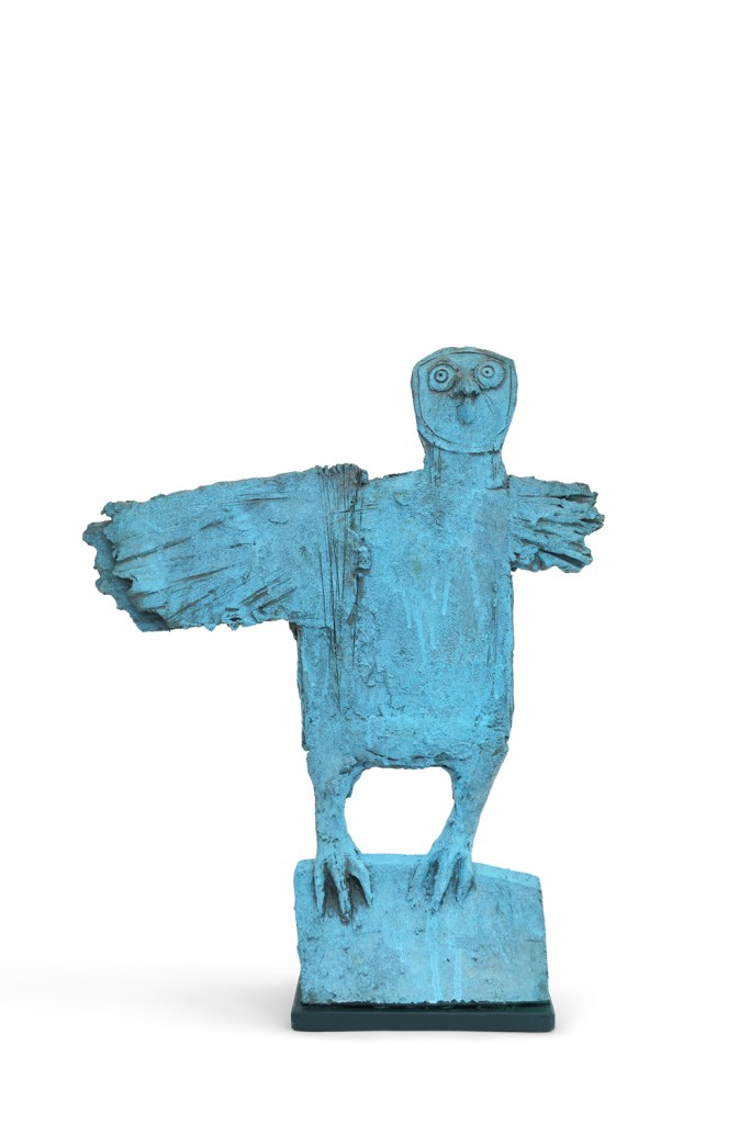 A blue ceramic sculpture depicting a stylized owl with outstretched wings, standing on a rectangular base.