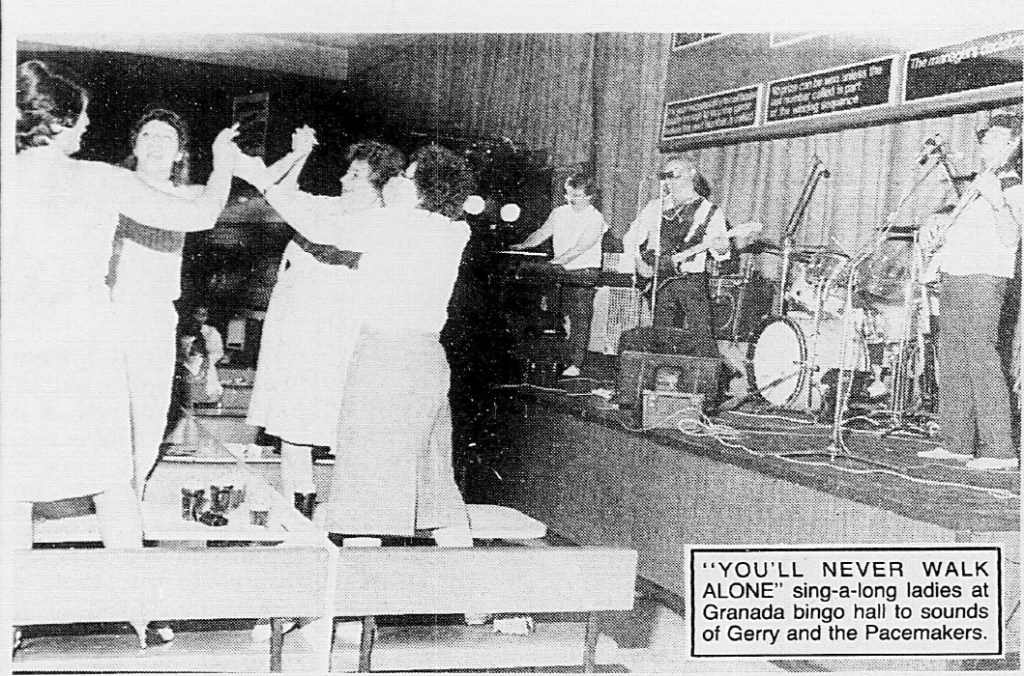 A group of women dancing and singing along at the Granada Bingo Hall, while a band performs on stage, featuring musicians playing various instruments.