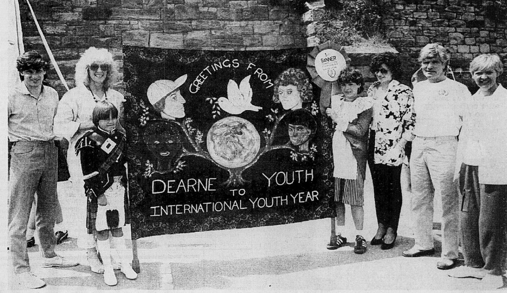 A group of people posing with a banner that reads 'Greetings from Dearne Youth International Youth Year'. The scene captures a moment from an event celebrating youth in 1985.