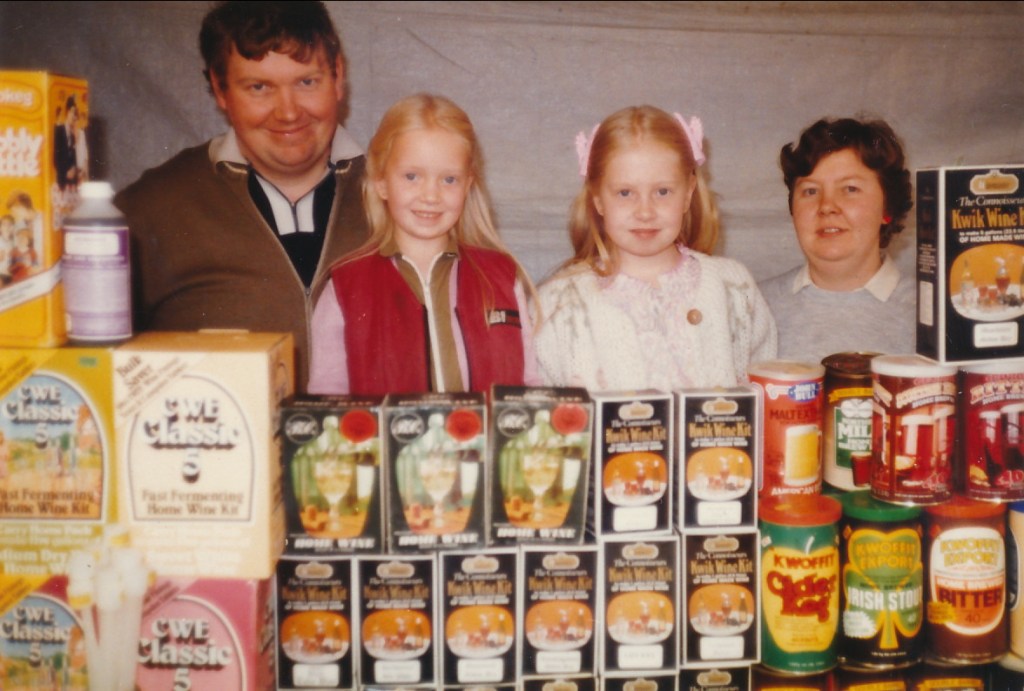 A family standing in front of various home brewing kits and canned beverages, smiling at the camera.
