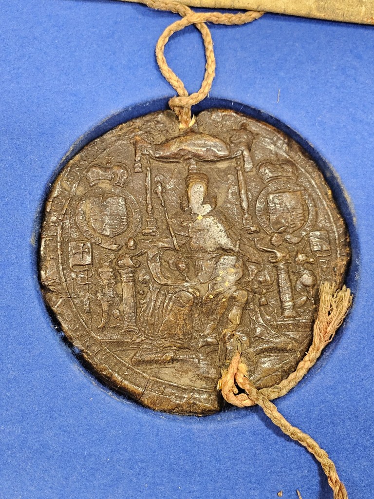 Close-up of a historic royal seal, featuring intricate details and a string attachment, resting on a blue background.