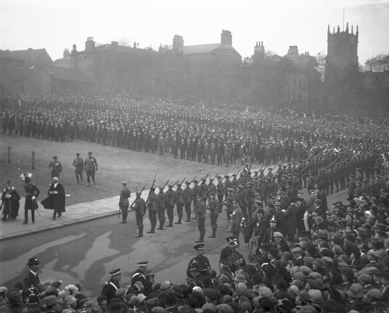 A historic black and white photograph of a large crowd gathered for a ceremonial event, featuring soldiers in formation and spectators lining the streets, likely during the unveiling of the Barnsley War Memorial.