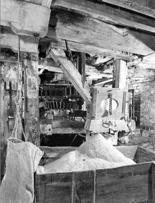 An interior view of Worsbrough Mill, showcasing the wooden machinery and a pile of flour on the floor.