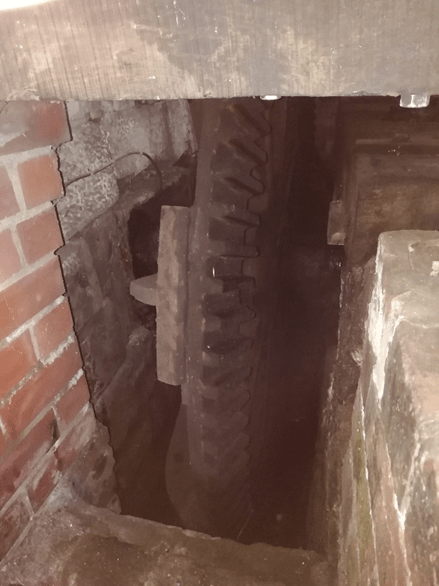 An interior view of Worsbrough Mill showing a large wooden cogwheel and surrounding brickwork, illustrating the machinery used in milling.