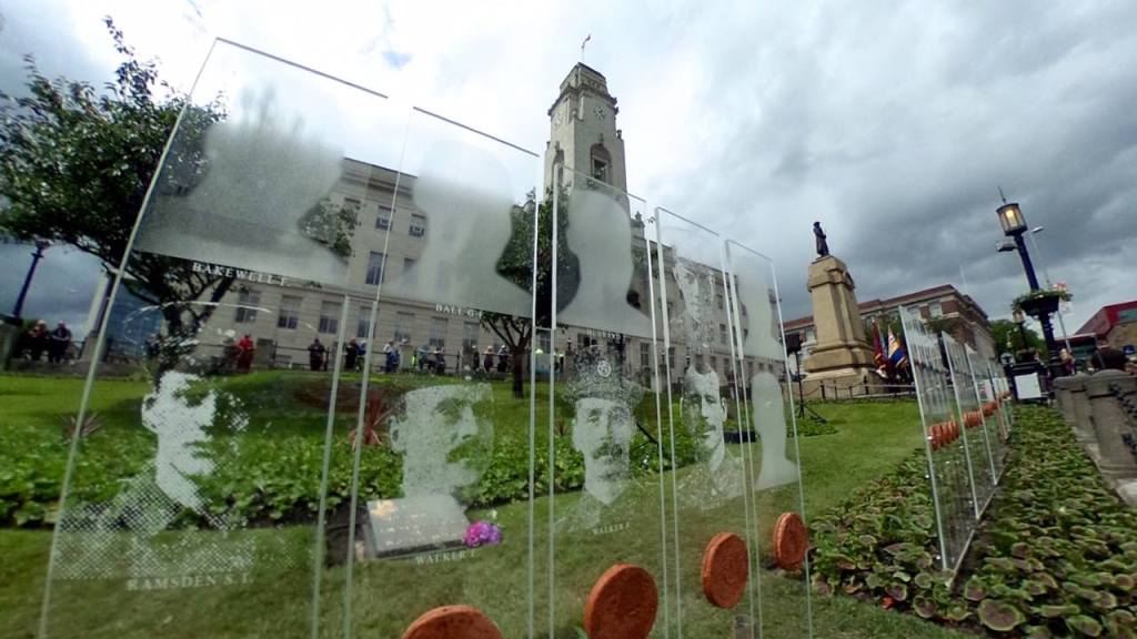View of Barnsley War Memorial with transparent panels displaying portraits of soldiers and the town hall in the background.