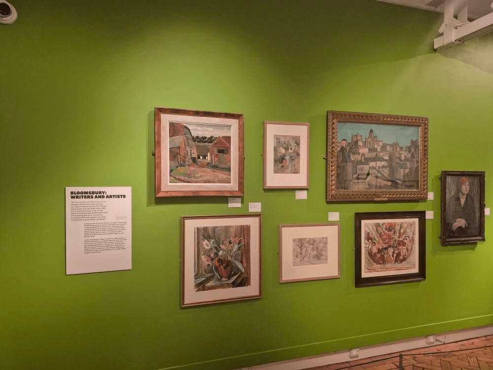 Artworks displayed in a gallery with a bright green wall, featuring multiple framed paintings and drawings, along with an informational plaque titled 'Bloomsbury: Writers and Artists'.