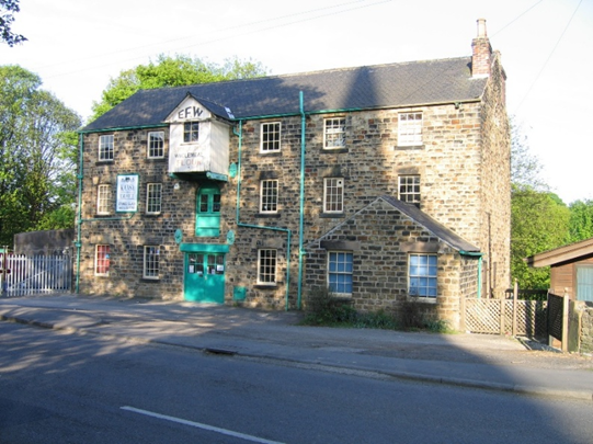 Historical Worsbrough Mill building featuring a stone facade, green highlights, and signage.