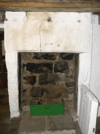 A historic fireplace made of stone and plaster, featuring a visible crack on the upper part of the mantel and a green box labeled 'MANTLE BOX' placed on the hearth.