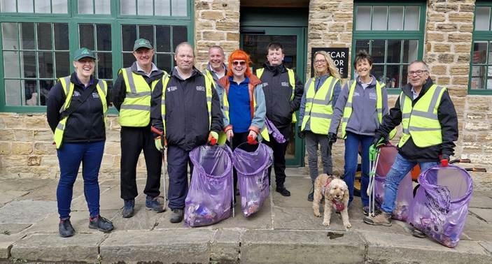 A group of volunteers wearing high-visibility vests, standing in front of a building, holding bags filled with collected litter.