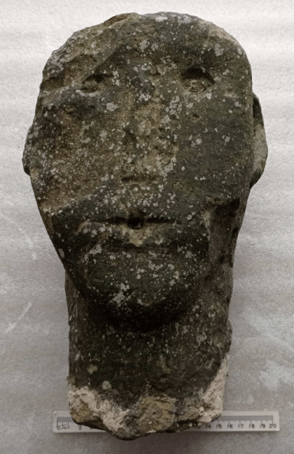Stone sculpture of a head with a worn, weathered surface, featuring minimal facial features.
