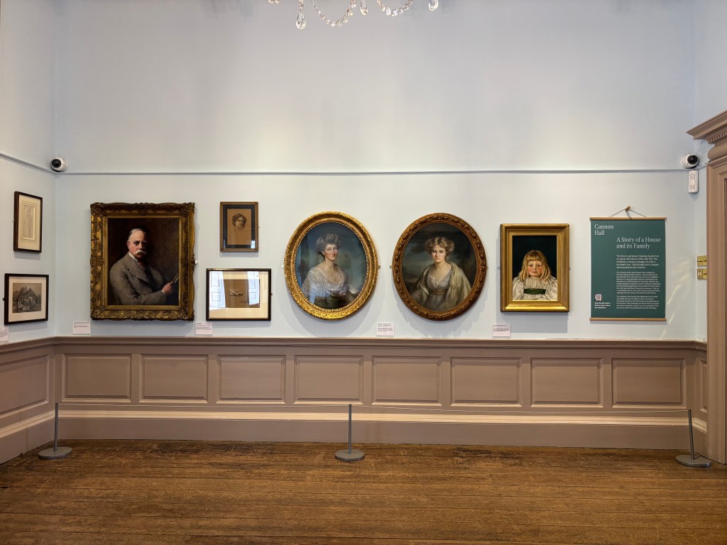 An art gallery wall featuring several framed portraits, including a prominent male figure on the left and three women in round frames, accompanied by an information panel on the right.
